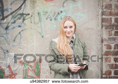 Stock Photo - Young woman using smartphone by graffiti wall. Fotosearch