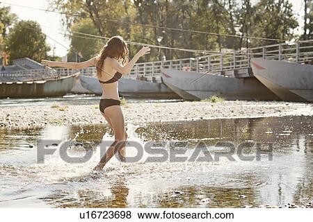 Stock Photo - Young woman wearing a bikini splashing and playing in river. Fotosearch