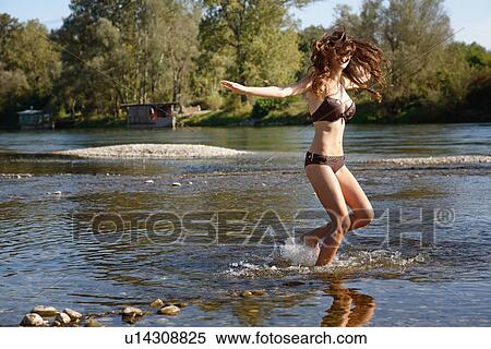 Stock Photography - Young woman wearing a bikini splashing and playing in river. Fotosearch
