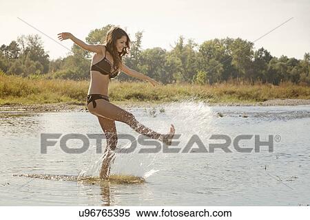 Stock Photography - Young woman wearing a bikini splashing and playing in river. Fotosearch