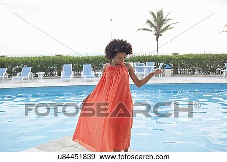 Stock Photo - "Young woman wearing orange dress at hotel poolside, Rio De Janeiro, Brazil". Fotosearch