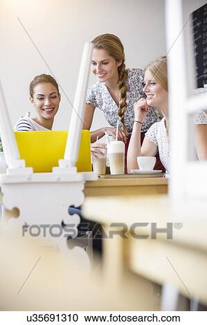 Stock Image - Young women smiling looking at laptop. Fotosearch