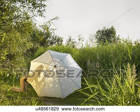 Stock Photo - Young women wearing bikini kneeling behind sunlit garden parasol. Fotosearch