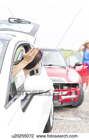 Stock Image - Angry woman gesturing while talking to female crashing car on road. Fotosearch