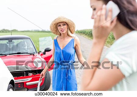 Angry woman looking at female using cell phone by damaged cars on road View Large Photo Image Picture - Angry woman looking at female using cell phone by damaged cars on road. Fotosearch