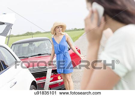 Angry woman standing by damaged cars with female using cell phone in foreground View Large Photo Image Stock Image - Angry woman standing by damaged cars with female using cell phone in foreground. Fotosearch