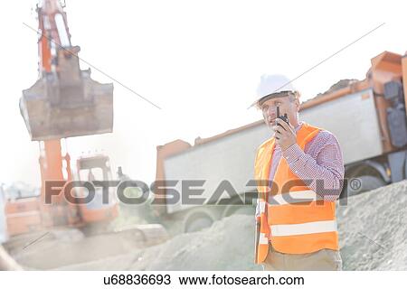 Stock Image - Architect using walkie-talkie while working at construction site. Fotosearch