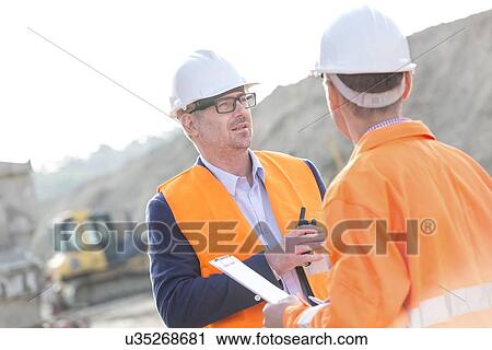 Architects discussing at construction site on sunny day View Large Photo Image Stock Image - Architects discussing at construction site on sunny day. Fotosearch