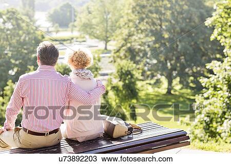 Back view of middle-aged couple relaxing on park bench View Large Photo Image Stock Image - Back view of middle-aged couple relaxing on park bench. Fotosearch