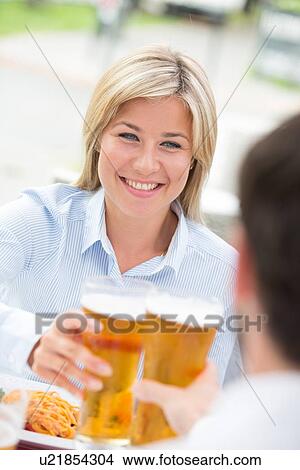 Picture - Beautiful businesswoman toasting beer glass with male colleague at restaurant. Fotosearch