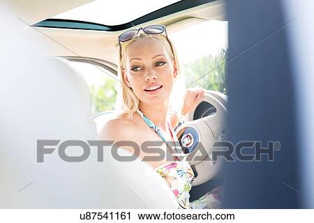 Beautiful woman looking back while driving car View Large Photo Image Stock Image - Beautiful woman looking back while driving car. Fotosearch
