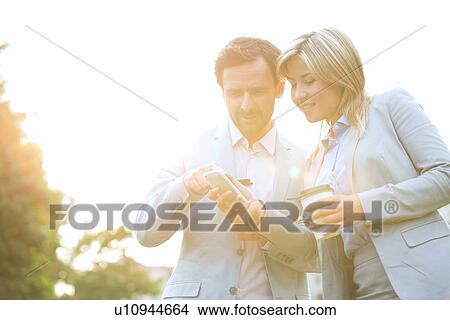 Business couple conversing while using cell phone on sunny day View Large Photo Image Picture - Business couple conversing while using cell phone on sunny day. Fotosearch