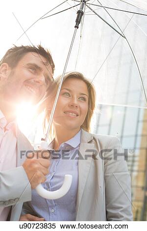 Business couple looking away while standing under umbrella on sunny day View Large Photo Image Stock Photography - Business couple looking away while standing under umbrella on sunny day. Fotosearch