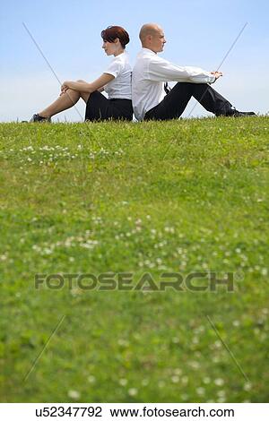 Stock Image - Business couple sitting back to back on grass. Fotosearch