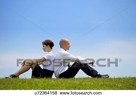Stock Photo - Business couple sitting back to back on grass. Fotosearch