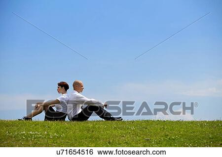 Business couple sitting back to back on grass View Large Photo Image Stock Photograph - Business couple sitting back to back on grass. Fotosearch