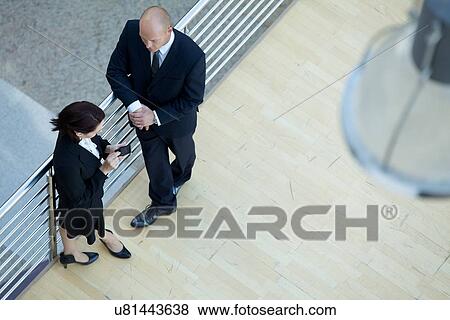 Stock Photo - Business executives standing together while businesswoman using mobile phone. Fotosearch