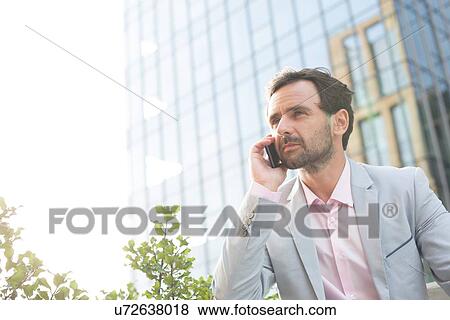 Stock Photo - Businessman answering mobile phone outside office building. Fotosearch