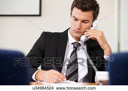 Businessman conversing on landline phone while writing on paper View Large Photo Image Picture - Businessman conversing on landline phone while writing on paper. Fotosearch