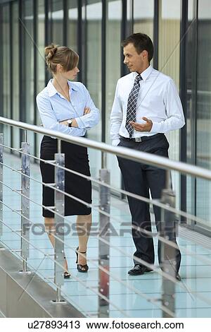 Stock Image - Businessman conversing with businesswoman at corridor. Fotosearch