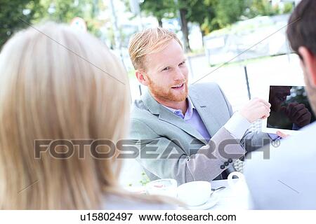 Stock Photo - Businessman discussing over digital tablet with colleagues at sidewalk cafe. Fotosearch