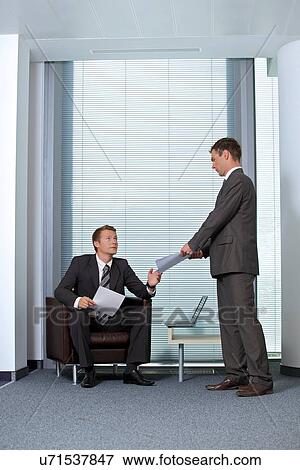 Businessman giving paper to colleague in office View Large Photo Image Stock Photo - Businessman giving paper to colleague in office. Fotosearch