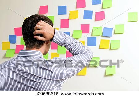 Stock Photograph - Businessman looking at wall of sticky notes with hands behind head. Fotosearch