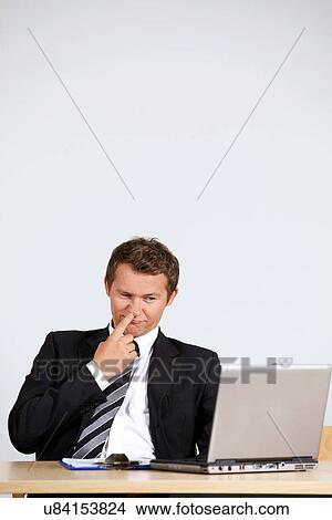 Picture - Businessman picking nose, looking at laptop in office. Fotosearch