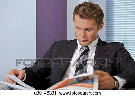 Stock Image - Businessman reading newspaper in office. Fotosearch