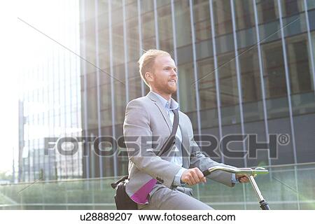 Businessman riding bicycle outside office building View Large Photo Image Stock Photo - Businessman riding bicycle outside office building. Fotosearch