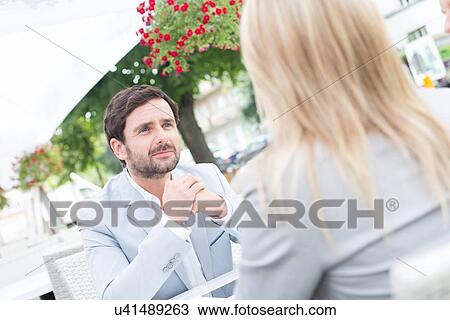 Stock Image - Businessman sitting with female colleague at sidewalk cafe. Fotosearch