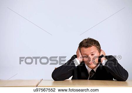 Stock Image - Businessman sitting with head in hands in office. Fotosearch