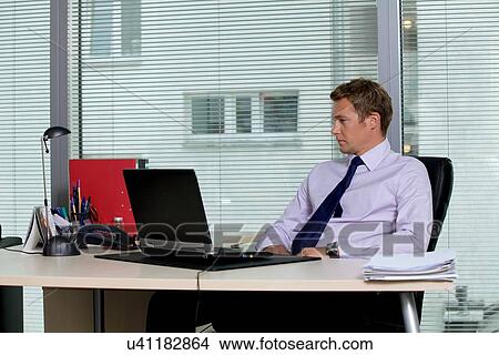 Businessman sitting with laptop at office View Large Photo Image Picture - Businessman sitting with laptop at office. Fotosearch