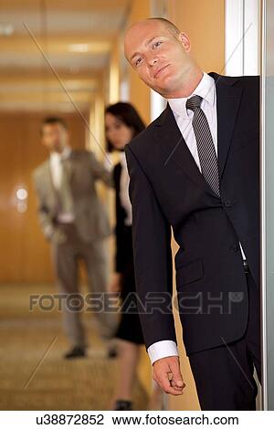 Stock Image - Businessman standing at door while colleagues in background. Fotosearch