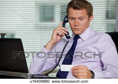 Businessman talking on telephone and looking at card in office View Large Photo Image Stock Image - Businessman talking on telephone and looking at card in office. Fotosearch
