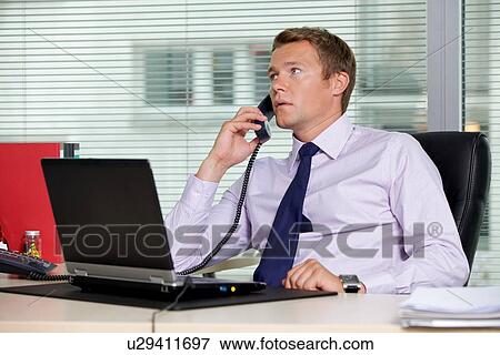 Businessman talking on telephone at office with laptop on table View Large Photo Image Stock Photo - Businessman talking on telephone at office with laptop on table. Fotosearch