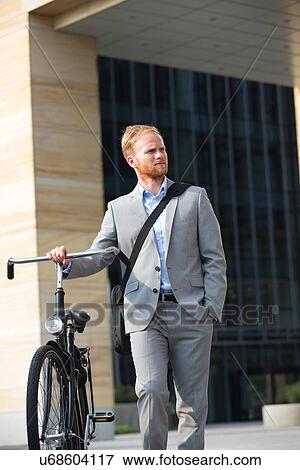 Businessman with bicycle looking away while standing outdoors View Large Photo Image Stock Photo - Businessman with bicycle looking away while standing outdoors. Fotosearch