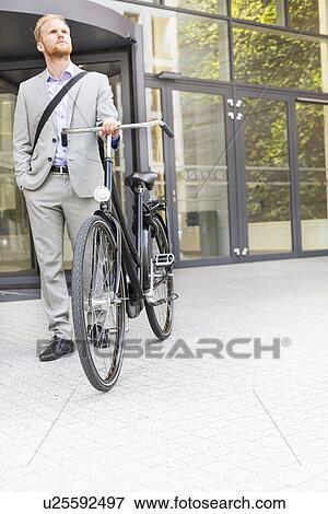 Businessman with bicycle standing outside office building View Large Photo Image Stock Photo - Businessman with bicycle standing outside office building. Fotosearch