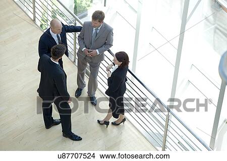 Picture - Businessmen and woman standing together by railing conversing. Fotosearch