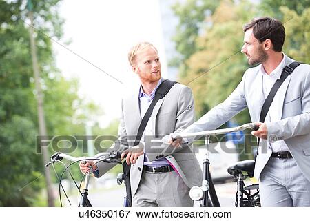 Businessmen looking at each other while holding bicycles outdoors View Large Photo Image Stock Photo - Businessmen looking at each other while holding bicycles outdoors. Fotosearch