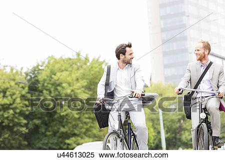 Stock Photography - Businessmen talking while riding bicycles outdoors. Fotosearch