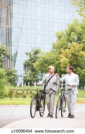 Picture - Businessmen talking while walking with bicycles on street. Fotosearch