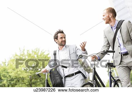 Businessmen talking while walking with bicycles outdoors View Large Photo Image Stock Photograph - Businessmen talking while walking with bicycles outdoors. Fotosearch