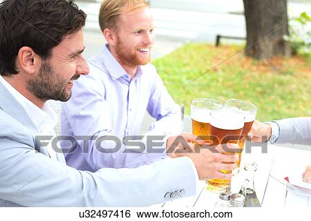 Stock Photograph - Businessmen toasting beer glasses with female colleague at outdoor restaurant. Fotosearch