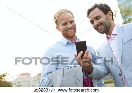 Stock Photo - Businessmen using mobile phone against clear sky. Fotosearch