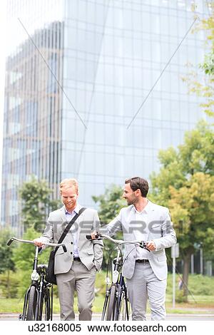 Stock Photography - Businessmen with bicycles walking against office building. Fotosearch