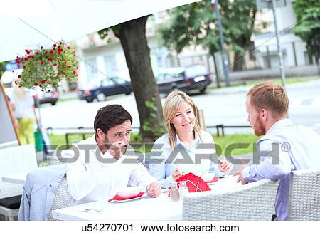 Stock Image - Businesspeople having food at outdoor restaurant. Fotosearch
