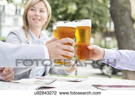 Stock Image - Businesspeople toasting beer glasses at outdoor restaurant. Fotosearch