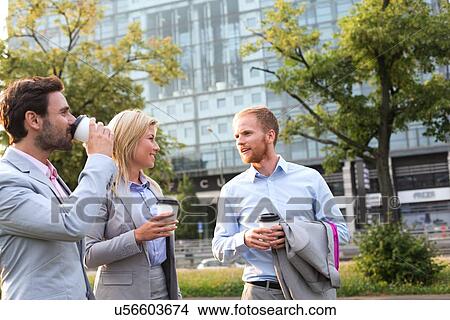 Picture - Businesspeople with disposable cups conversing in city. Fotosearch