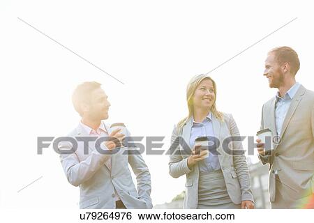 Businesspeople with disposable cups talking against clear sky on sunny day View Large Photo Image Stock Photograph - Businesspeople with disposable cups talking against clear sky on sunny day. Fotosearch